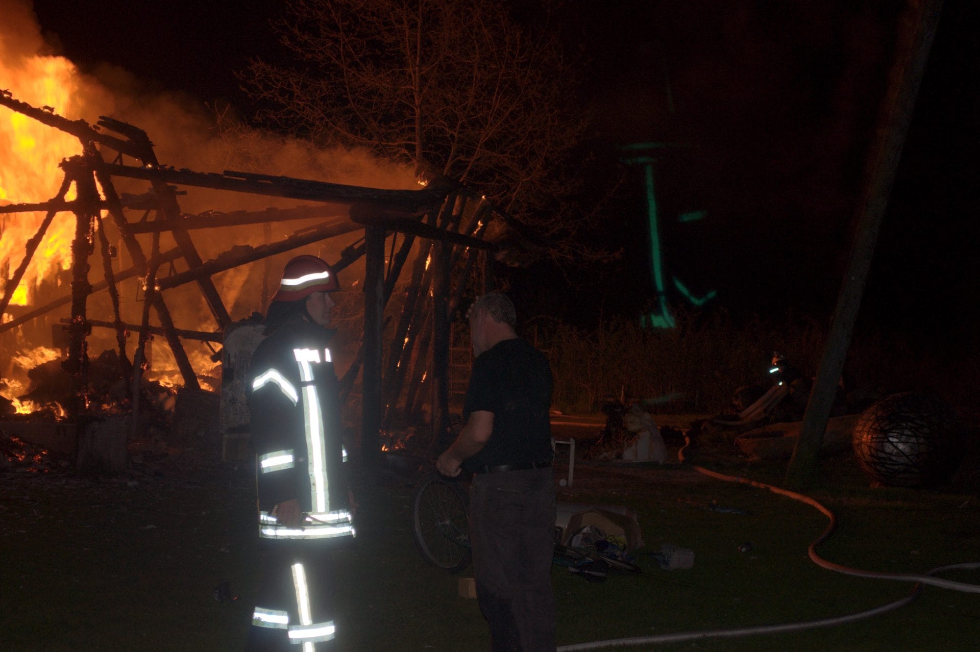 NIKON CORPORATION NIKON D5000 · 55 mm · f/5.6 · 1/60 s A nighttime scene with a large fire burning in the background, with a person wearing reflective gear standing in the foreground.