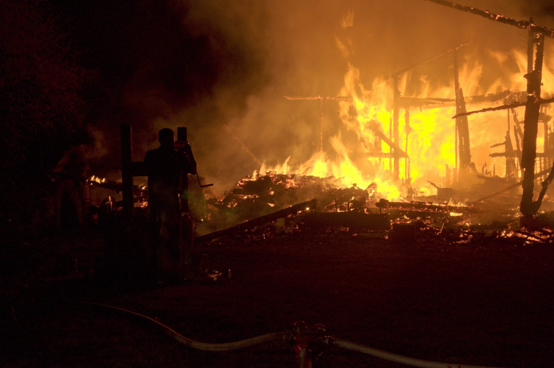 NIKON CORPORATION NIKON D5000 · 55 mm · f/5.6 · 1/25 s A nighttime scene of a large fire consuming a structure, with a firefighter using a hose to combat the flames.
