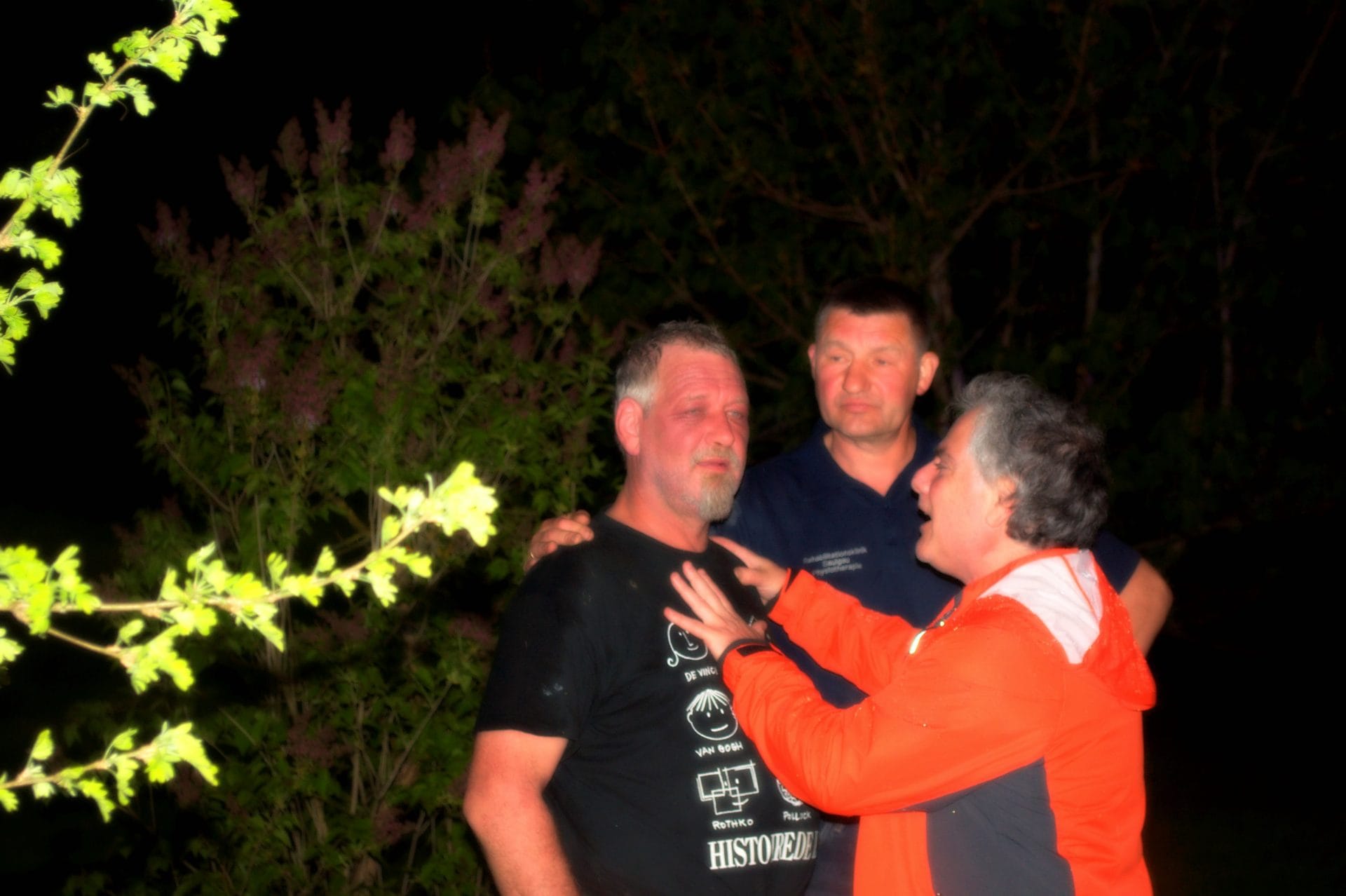 NIKON CORPORATION NIKON D5000 · 48 mm · f/5.3 · 1/60 s Three people are standing outside at night, with one person gesturing towards another.