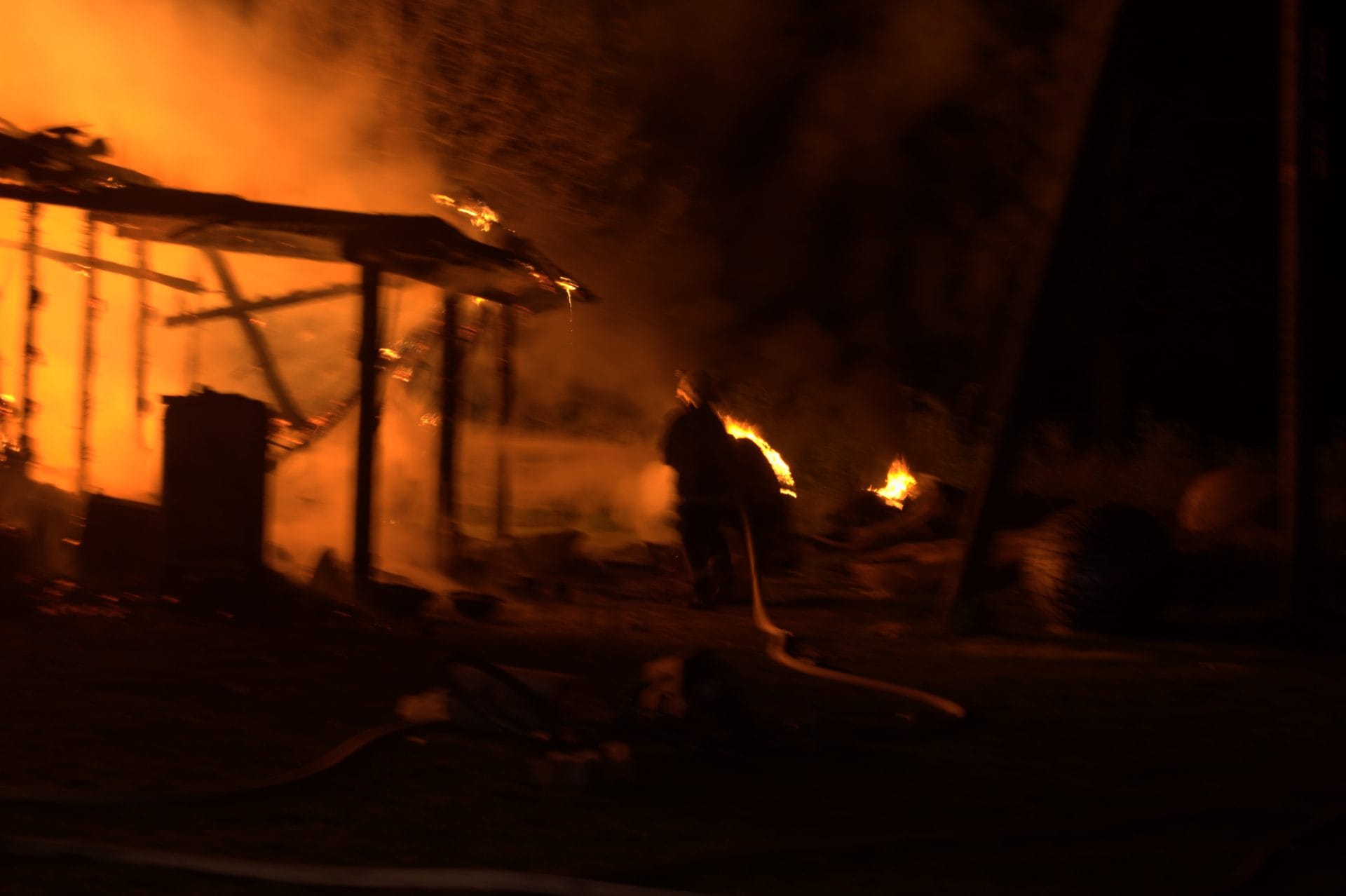A nighttime scene of a burning structure with flames and smoke visible.