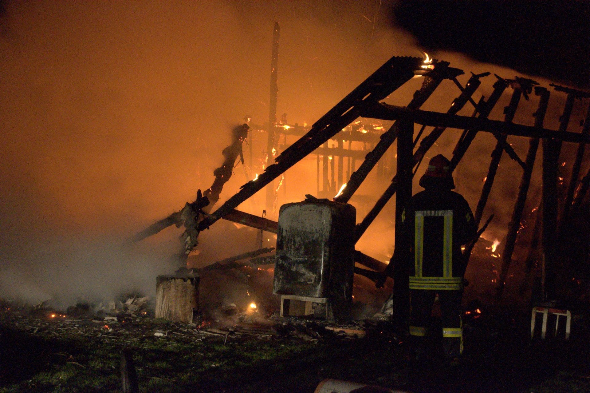 NIKON CORPORATION NIKON D5000 · 55 mm · f/5.6 · 1/6 s A nighttime scene of a fire at a structure, with a firefighter standing in the foreground.