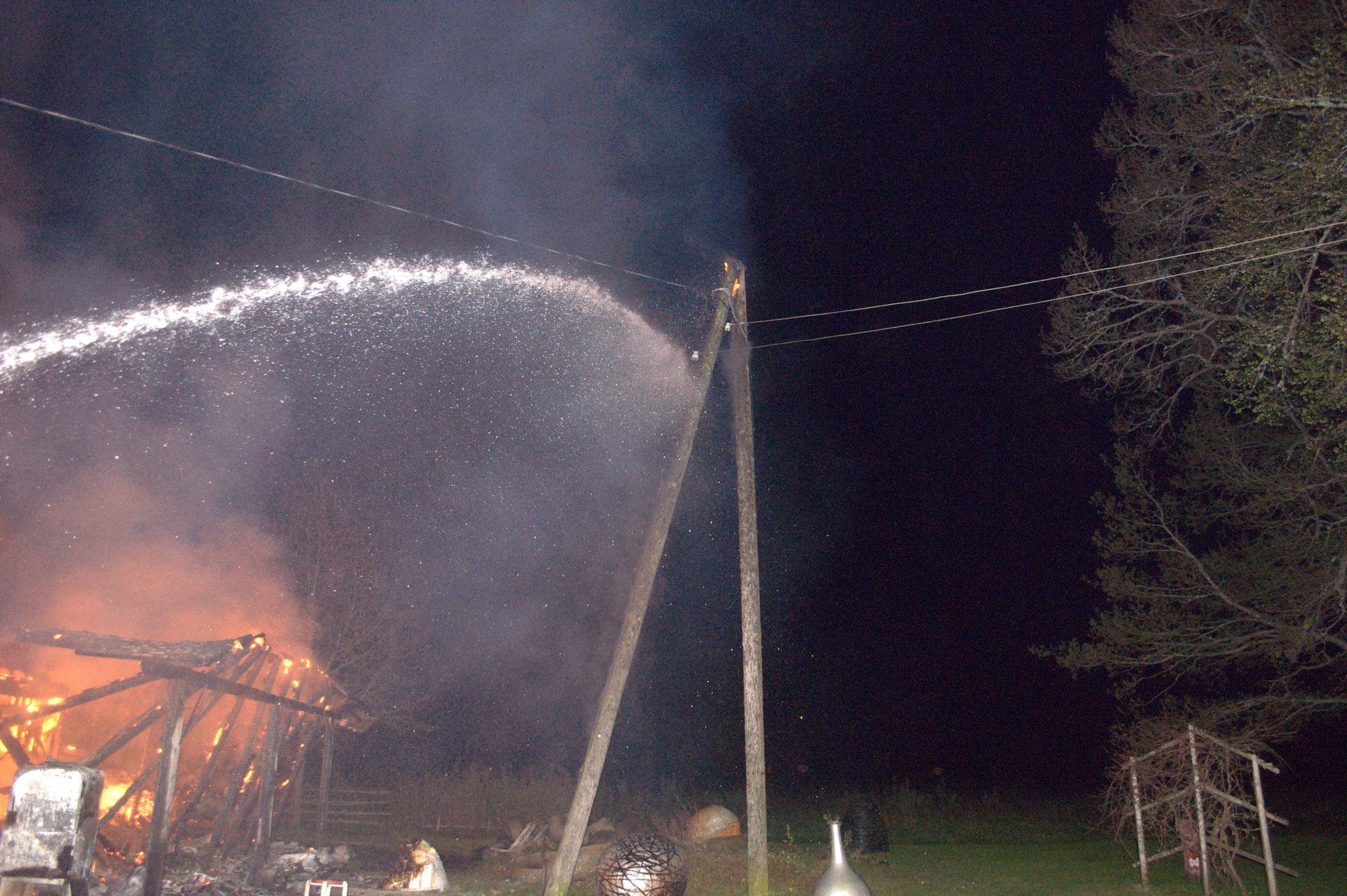 A nighttime scene of a fire being put out with a hose.